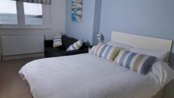 A bedroom with a large bed, a nightstand, a window with a view, and a painting on the wall.
