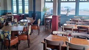 A restaurant interior with wooden tables and chairs, large windows, and hanging pendant lights. - The Paris Hotel (Helston)