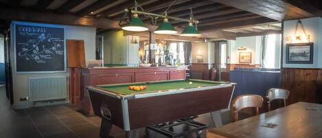 A pool table in a room with a high ceiling and exposed beams, a bar area with a chalkboard menu, and a billiards table.
