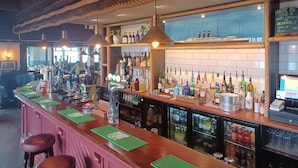 A bar area with a wooden counter, green placemats, and a variety of bottles and glasses. - The Paris Hotel (Helston)