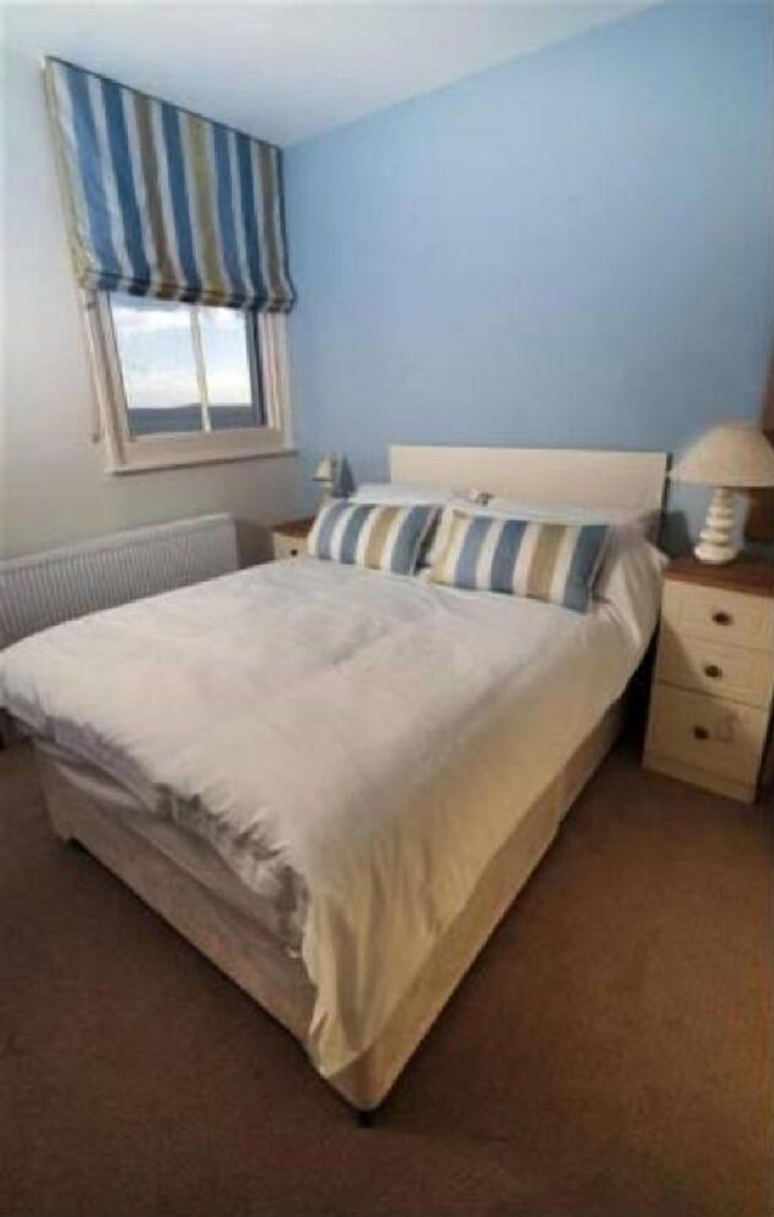 A bedroom with a bed, a nightstand, a lamp, and a window with curtains.
