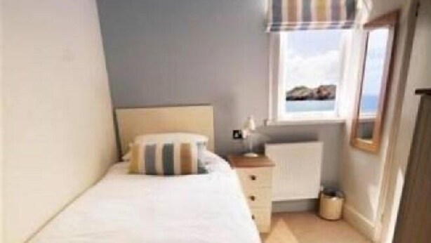 A small, neatly arranged bedroom with a single bed, a dresser, and a window with a view. - The Paris Hotel (Helston)
