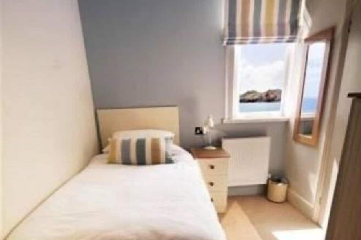 A small, neatly arranged bedroom with a single bed, a dresser, and a window with a view.