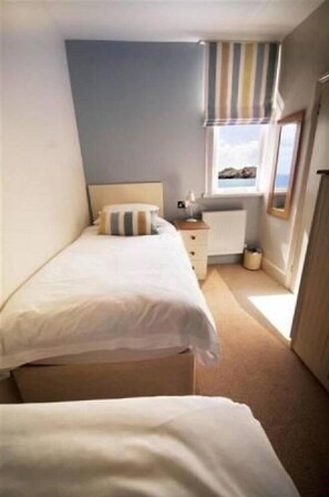 A small, neatly arranged bedroom with a single bed, a dresser, and a window with a view. - The Paris Hotel (Helston)