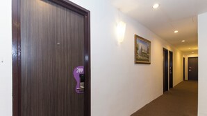 A hotel corridor with a wooden door, a number plaque, a wall-mounted light, and a framed picture.