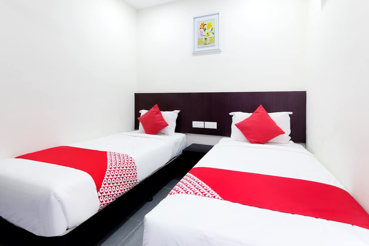 Una habitación de hotel con dos camas individuales, cada una con colcha roja y blanca, cabecero oscuro y un pequeño cuadro en la pared.