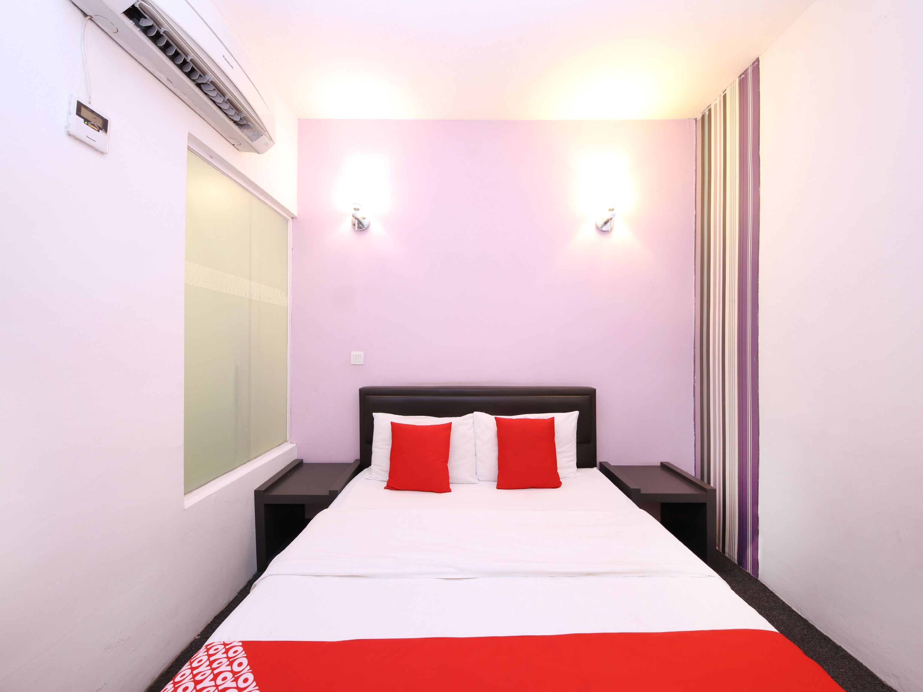 Una camera d'albergo con un letto, due comodini, una finestra e un condizionatore d'aria.