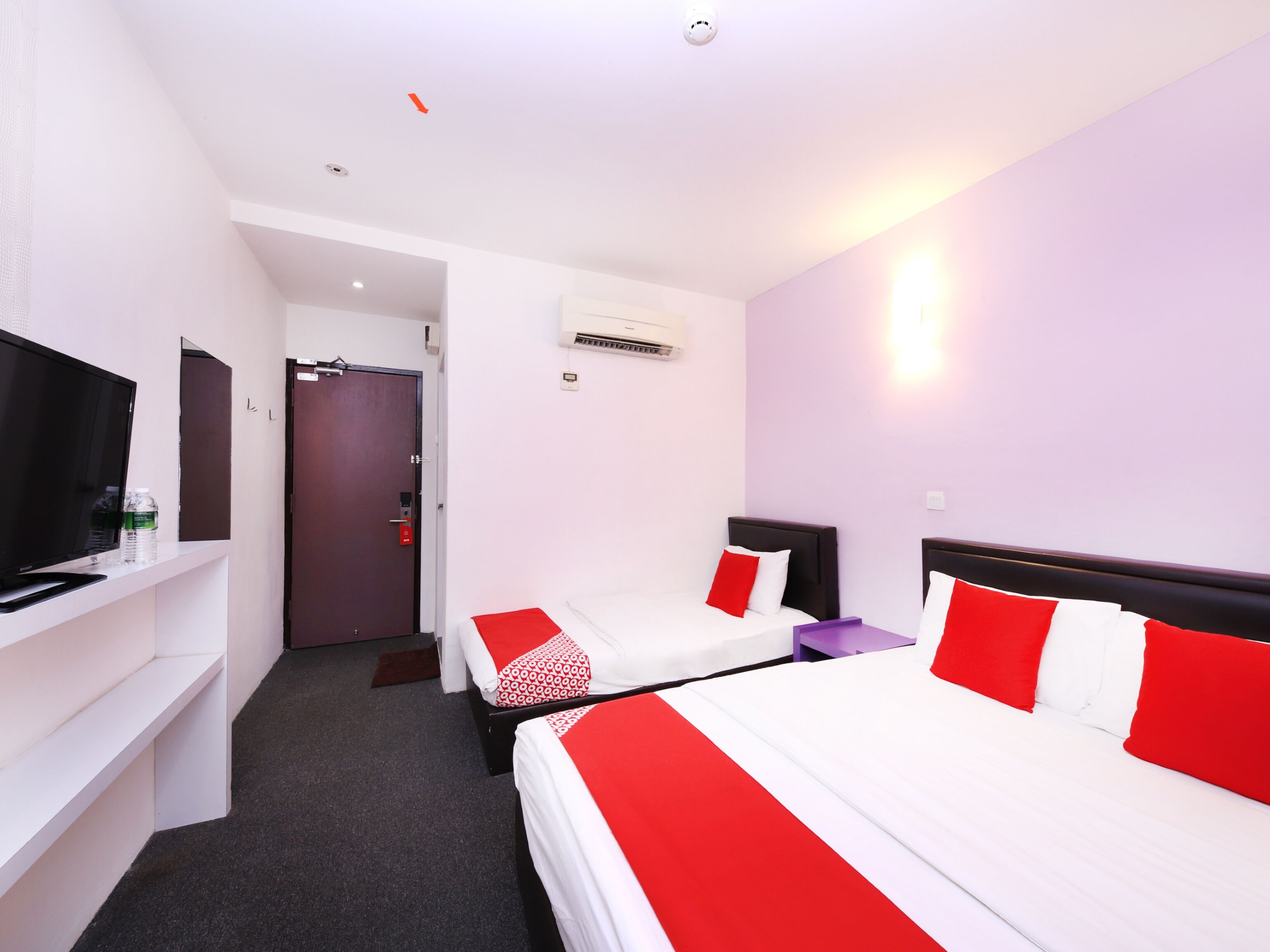 A hotel room with two beds, a TV, a desk, and an air conditioning unit.
