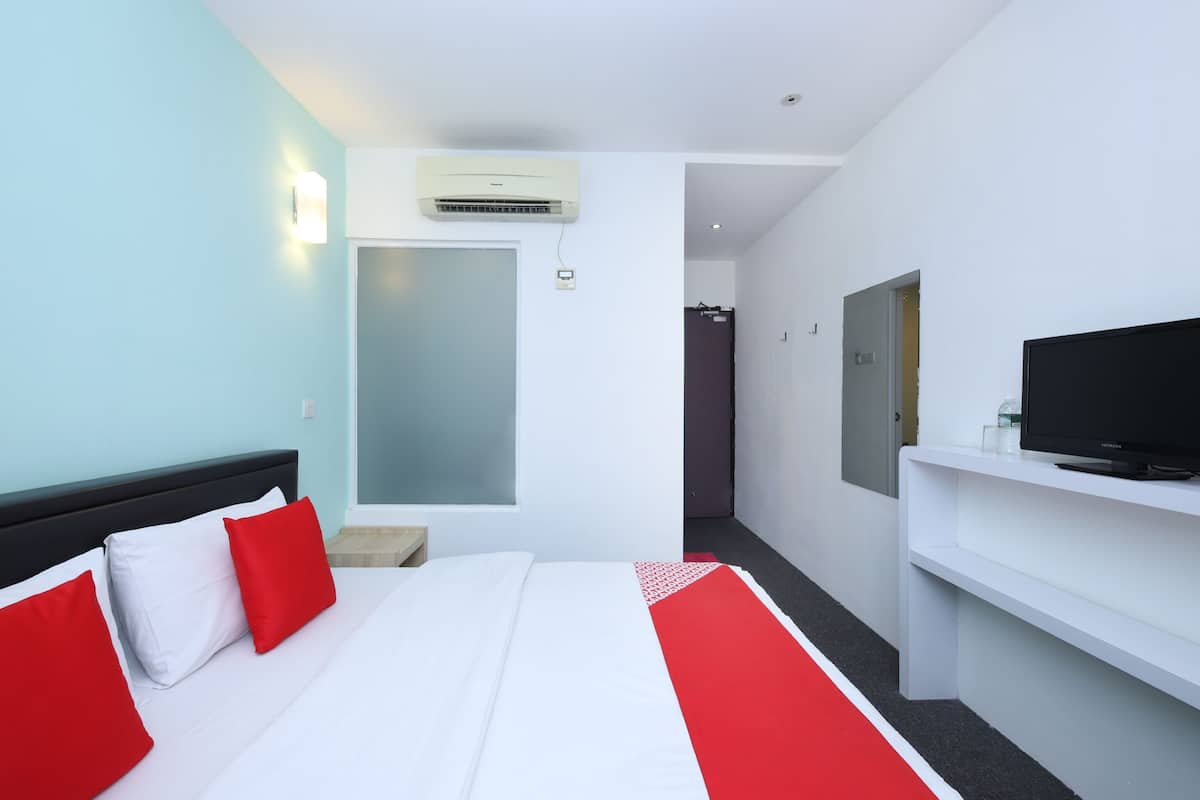 Una habitación de hotel con cama, televisión, aire acondicionado, una puerta y una mesita.