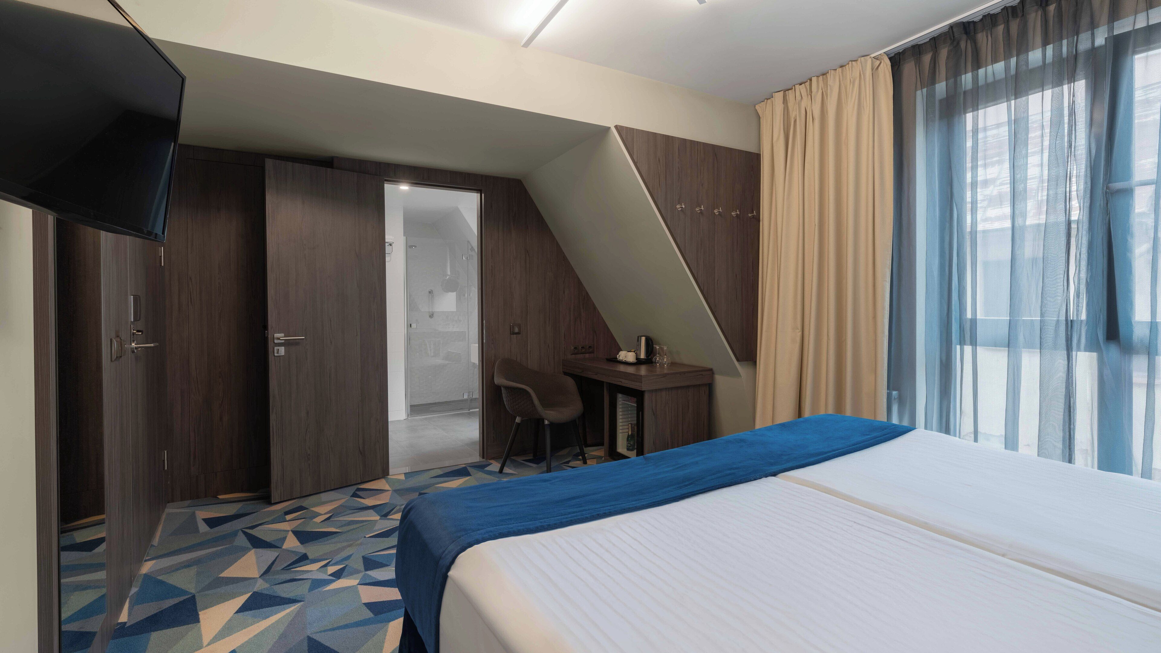A hotel room with a bed, a desk, a chair, a TV, and a bathroom.