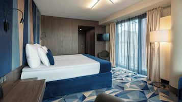 Habitación de hotel con cama, escritorio, silla, televisión y ventana con cortinas.