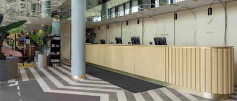 Una recepción moderna con una larga barra de mostrador, múltiples monitores de computadora y una vista despejada del piso superior a través de barandales de vidrio.