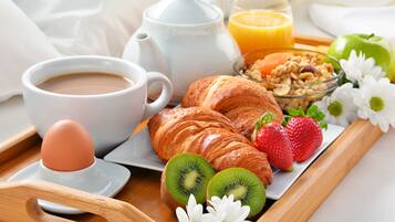 Aamiaistarjotin, jossa on croissantteja, mansikoita, kiivejä, keitetty kananmuna, kahvia, appelsiinimehua ja kulho täynnä mysliä.