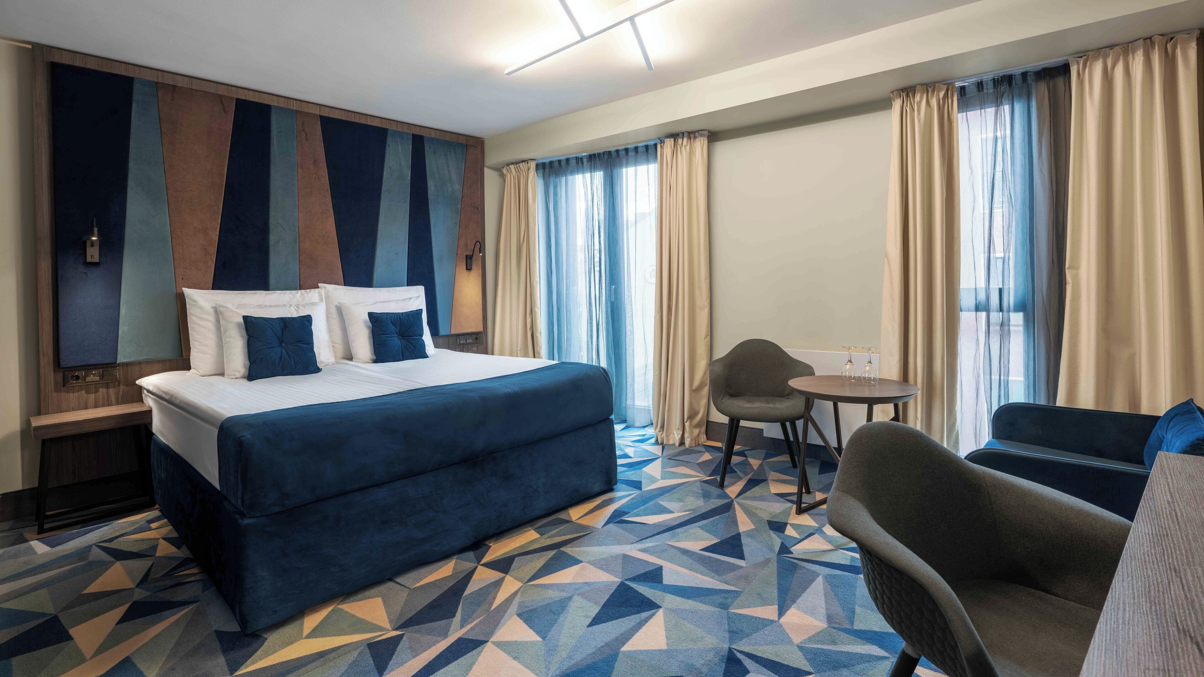 Una habitación de hotel con una cama grande, una mesita con dos vasos, una silla y un sofá.