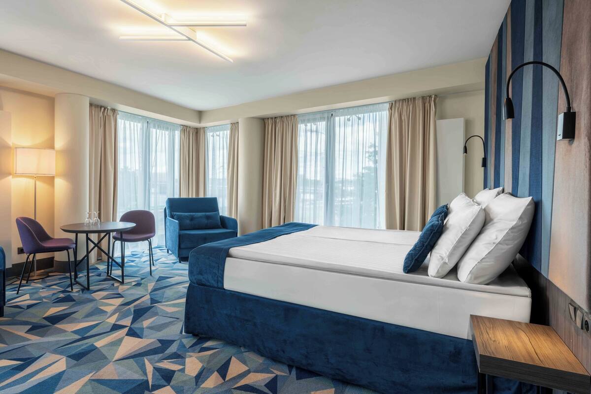 A hotel room with a large bed, two armchairs, a small table, and a lamp.