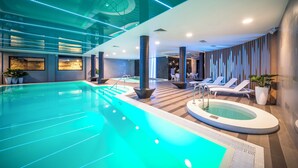 A modern indoor swimming pool with a jacuzzi, lounge chairs, and potted plants.