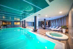 A modern indoor swimming pool with a jacuzzi, lounge chairs, and potted plants.