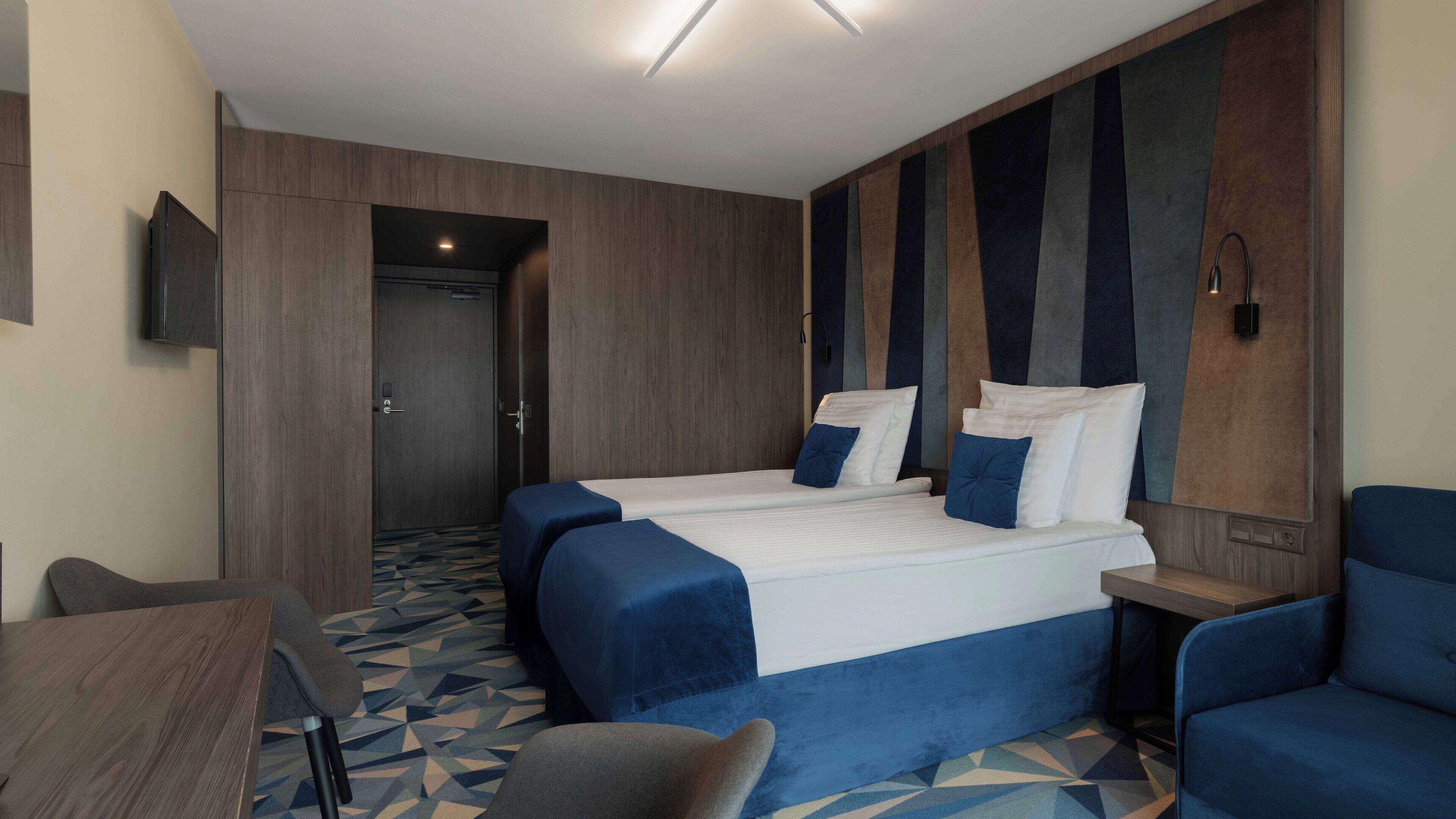 A hotel room with two beds, a desk, and a chair.