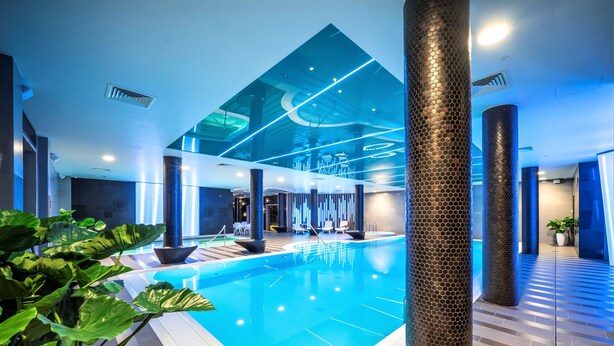 An indoor swimming pool with a modern design, surrounded by large columns and potted plants.