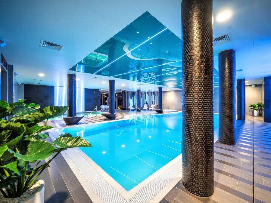 An indoor swimming pool with a modern design, surrounded by large columns and potted plants.