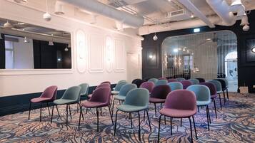 A conference room with rows of chairs, a patterned carpet, and a modern ceiling with exposed ductwork.