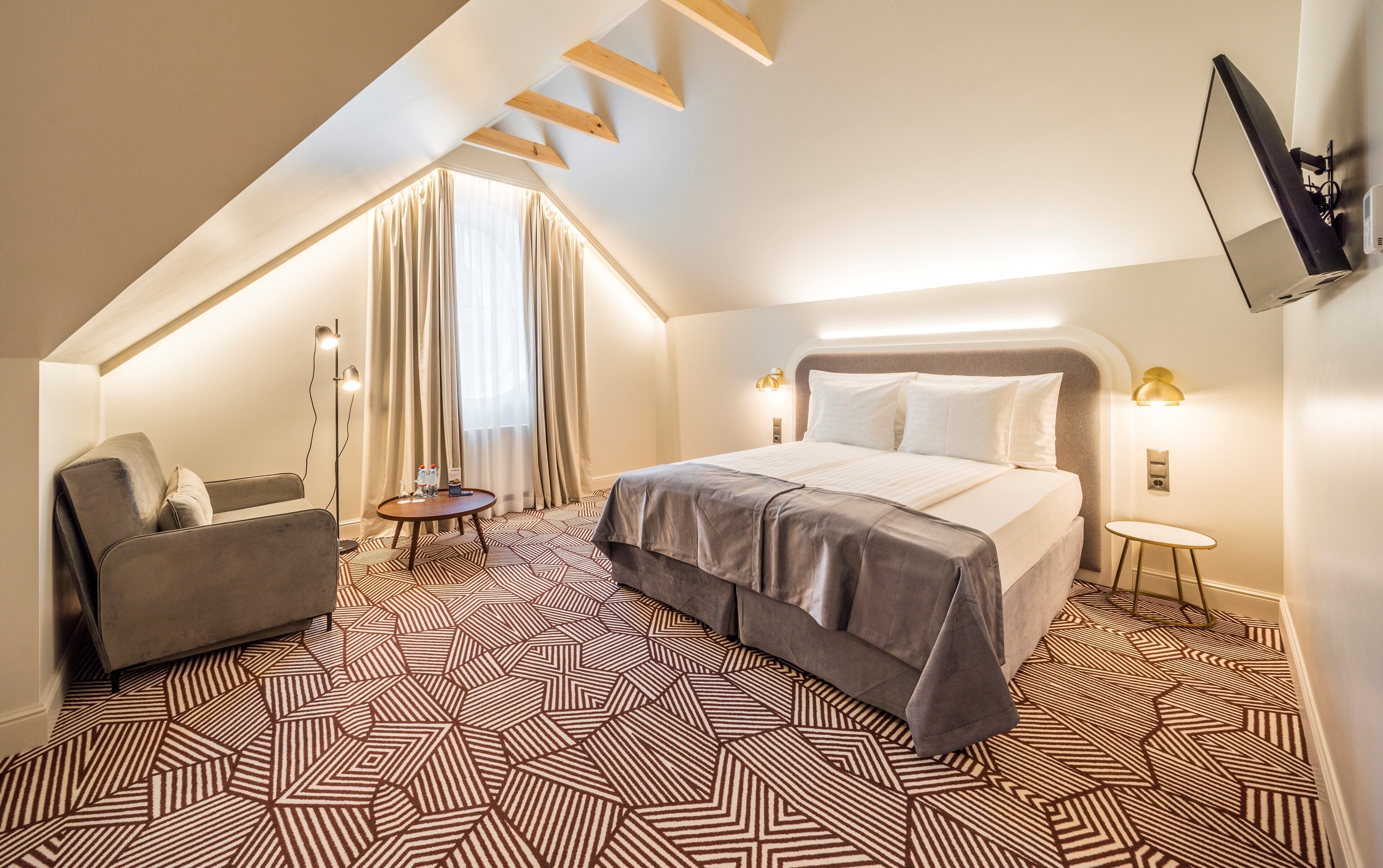 Een moderne hotelkamer met een groot bed, een bank, een klein tafeltje en een aan de muur bevestigde televisie.