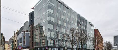 A modern hotel with a glass facade, located at a street corner with a pedestrian walkway.