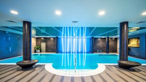 An indoor swimming pool with a modern design, featuring a central water feature, two large columns, and a patterned floor.