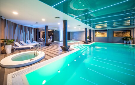 A modern indoor swimming pool with lounge chairs and a hot tub area.