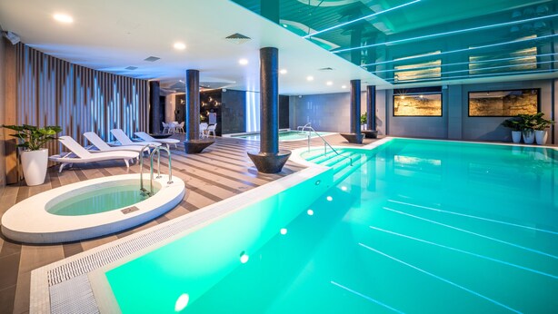A modern indoor swimming pool with lounge chairs and a hot tub area. - Wellton Riverside SPA Hotel (Riga)