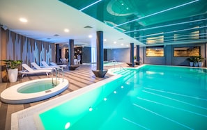 A modern indoor swimming pool with lounge chairs and a hot tub area.