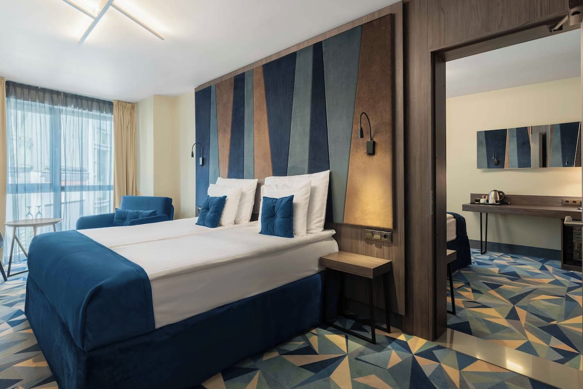 A hotel room with a large bed, a desk, a chair, and a bathroom visible through an open door.
