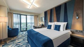 A hotel room with a large bed, a desk, a chair, and a view of the outdoors.