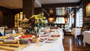 A banquet table with various food items and a floral centerpiece in a well-lit room with wooden floors and large windows.