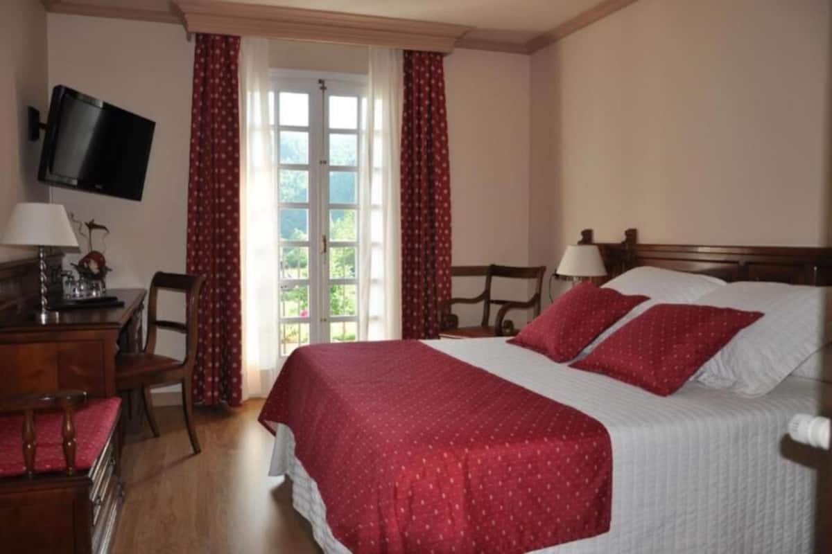 Quarto com cama, duas mesas de cabeceira, TV fixada na parede e janela com cortinas.
