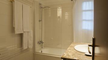 A modern bathroom with a glass-enclosed shower, a bathtub, and a marble countertop with a sink.
