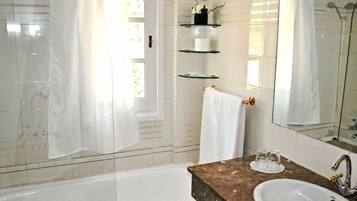 A bathroom with a bathtub, a sink, a mirror, and shelves with toiletries.