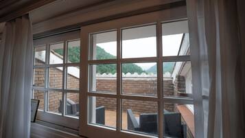 Blick durch ein Fenster mit mehreren Fensterscheiben auf eine Ziegelwand und einen Außenbereich mit Sitzgelegenheiten und Stühlen.