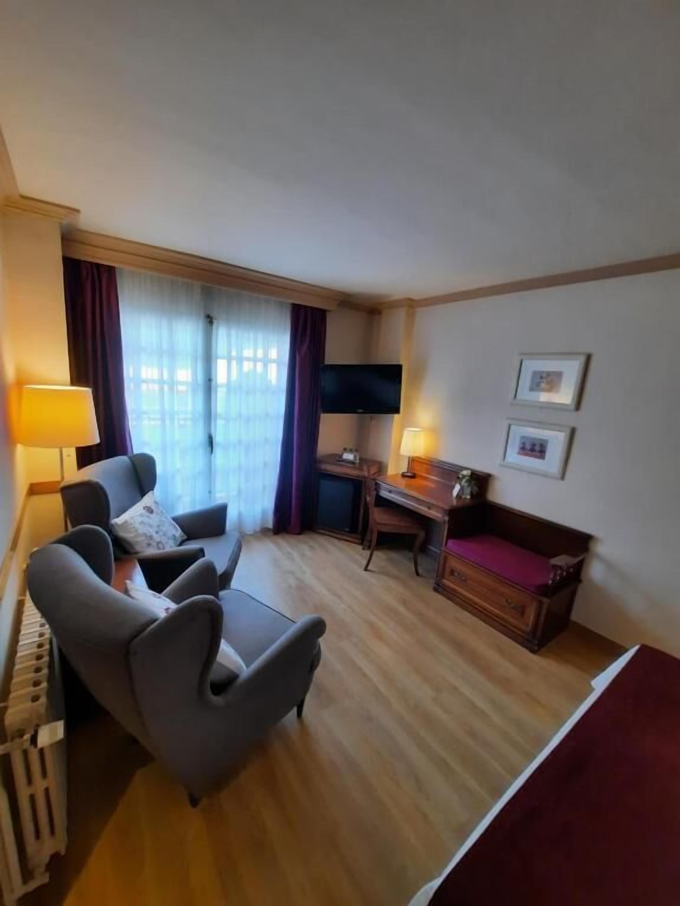 A hotel room with a wooden floor, a sofa, a desk, a TV, and two lamps.