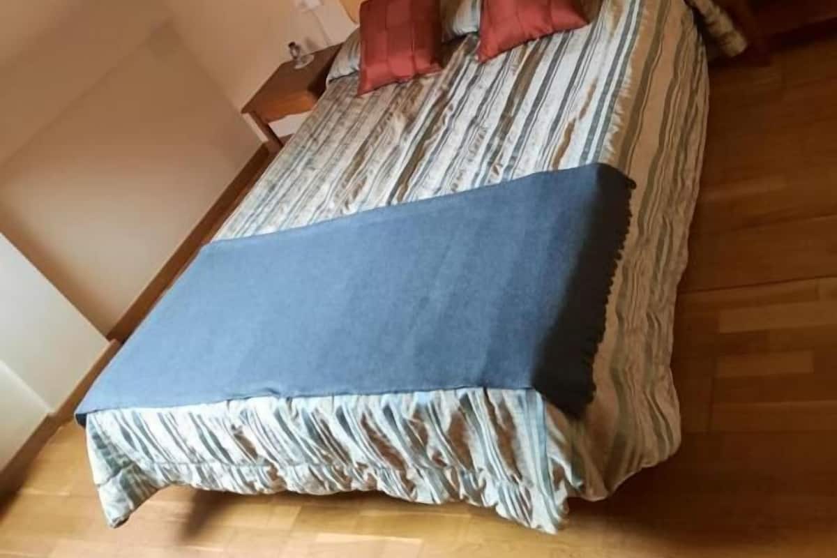 Um quarto com uma cama, almofadas, uma mesa de cabeceira e uma luminária.