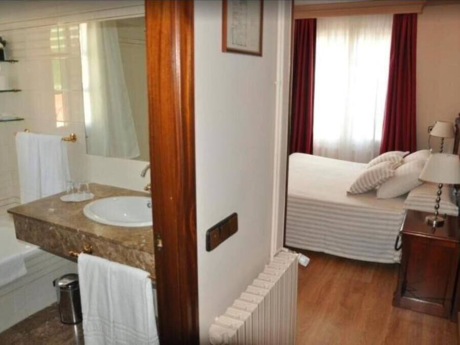Ein Hotelzimmer mit Bad, einem Bett, einem Nachttisch und einem Fenster mit Vorhängen.