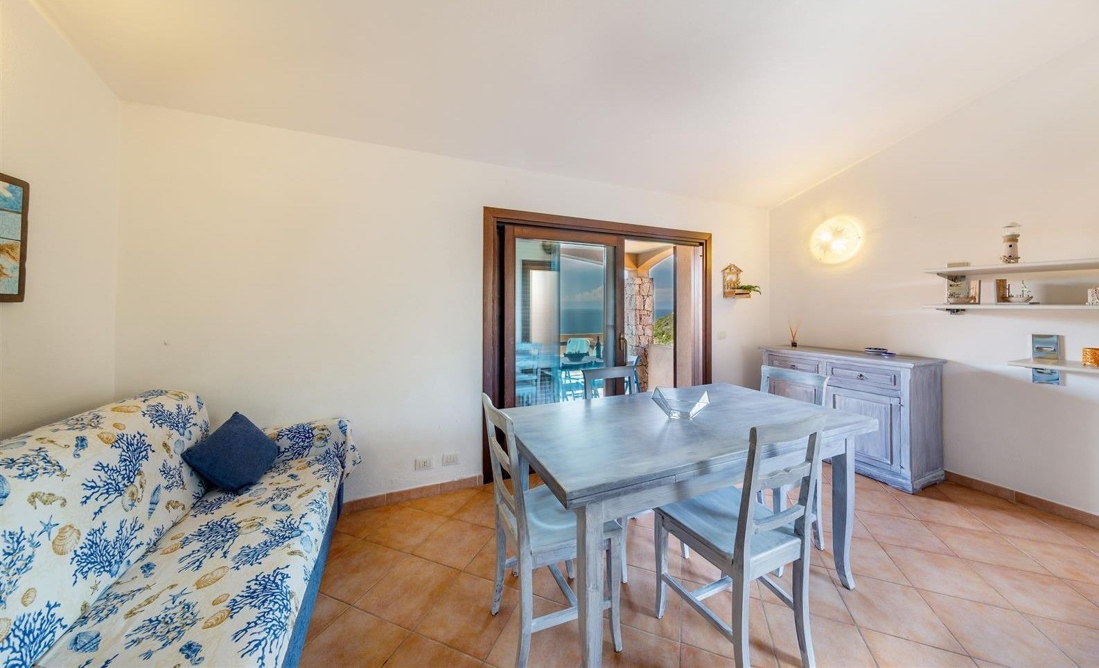 A compact living space with a dining area, a sofa with a patterned cover, and a kitchen area with a countertop and cabinets.
