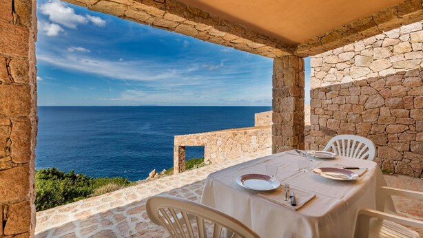 A stone patio with a table set for two, overlooking a coastal view.