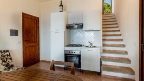 A compact kitchen with a gas stove, oven, and white cabinets. A wooden door and a dining table with chairs are visible.