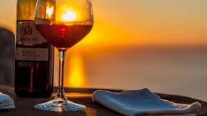 A bottle of Sentidu Monica di Sardegna wine and a glass on a table with a sunset view.