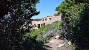 A stone building with a pathway leading to it, surrounded by dense greenery. - Villetta Nuvola Azzurra (Trinità d'Agultu e Vignola)