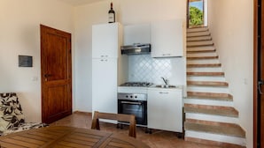 A compact kitchen with a gas stove, oven, and white cabinets. There's a wooden door and a staircase with beige steps. - Villetta Nuvola Azzurra (Trinità d'Agultu e Vignola)