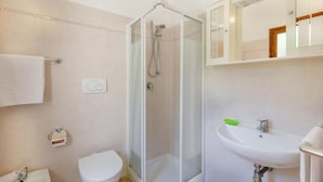 A bathroom with a toilet, a sink, a shower enclosure, and a mirror. - Villetta Nuvola Azzurra (Trinità d'Agultu e Vignola)