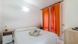 A bedroom with a bed, a nightstand, a lamp, a desk, and an orange curtain.