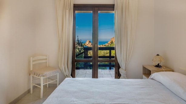A bedroom with a bed, a chair, a nightstand, and a view of a rocky landscape through a glass door.